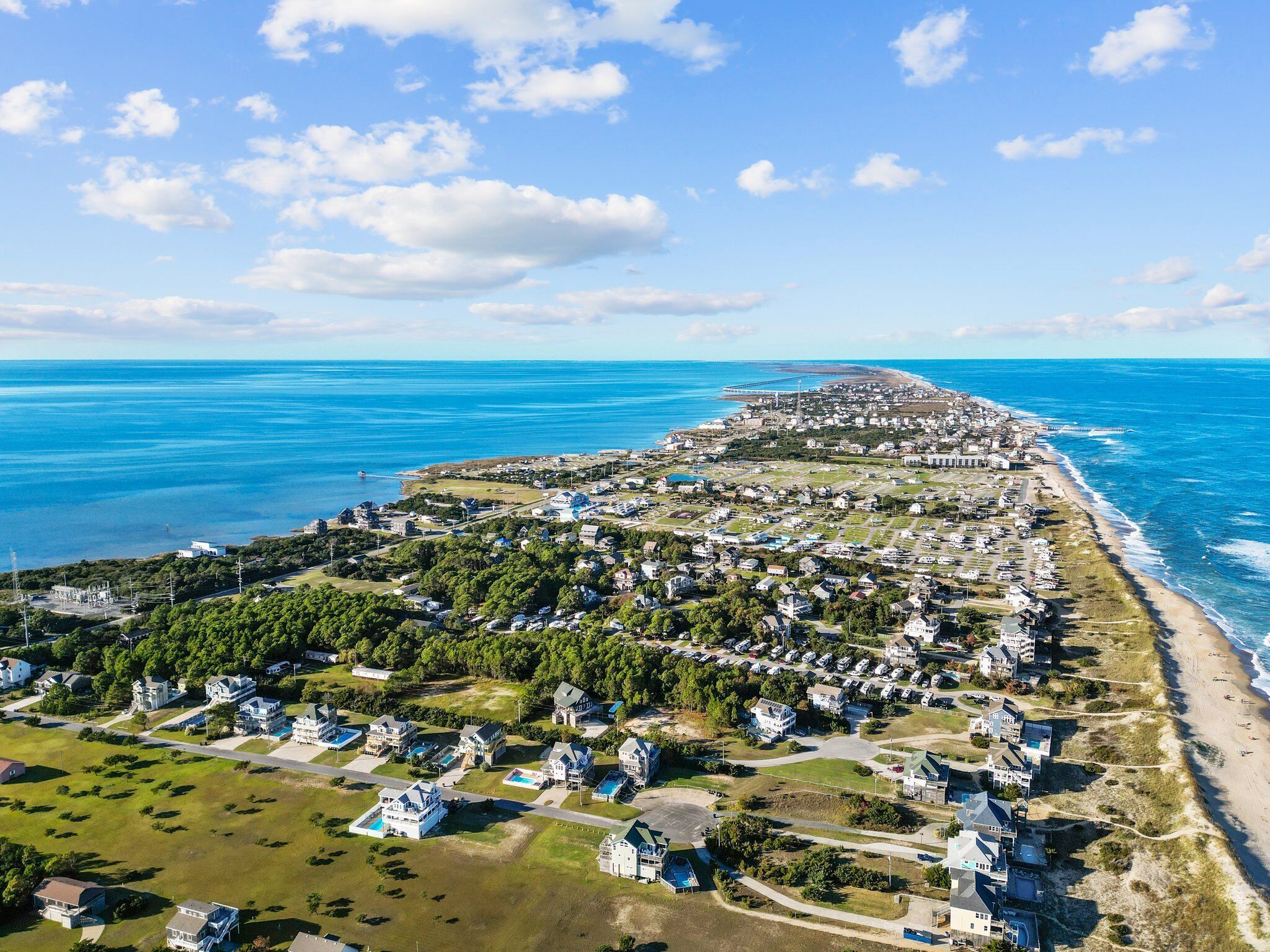 An aerial view of a coastal town with residential areas, a beach, and a bridge connecting to the mainland.