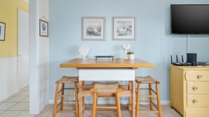 Una habitación con una mesa de madera, dos sillas, un armario pequeño blanco y un televisor.