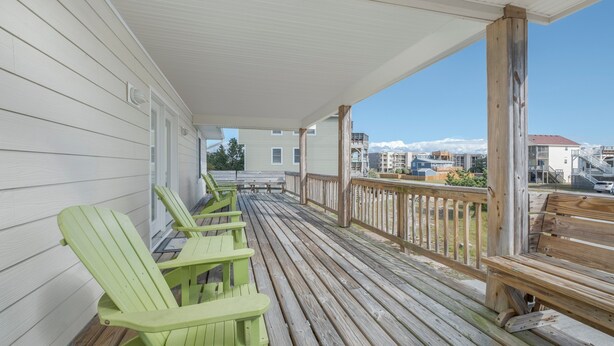 Una terraza de madera con sillas Adirondack verdes y barandilla, con vistas a una zona residencial con casas y montañas.