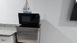 A compact kitchen with a stainless steel refrigerator and a microwave on top.