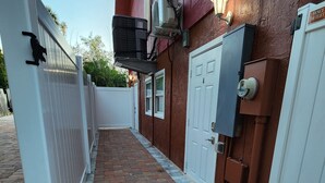A narrow brick pathway leading to a building with a red exterior, a white door, and a white fence on one side.