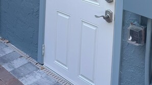 A white door with a keypad lock, a small window above it, and a utility box to the right.