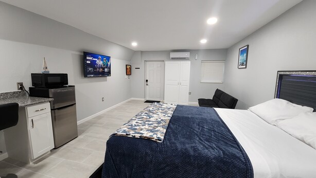 A bedroom with a bed, a desk with a microwave, a TV, and a door.