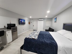 Ett sovrum med en säng, ett skrivbord med en mikrovågsugn, en tv och en dörr.