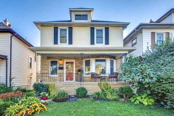 A two-story house with a front porch, a small garden, and a mailbox. - The Hipster House (Windsor)