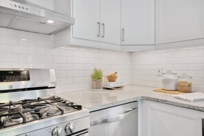 A modern kitchen with white cabinetry, a stainless steel stove, and a digital clock displaying 1:46. - The Hipster House (Windsor)