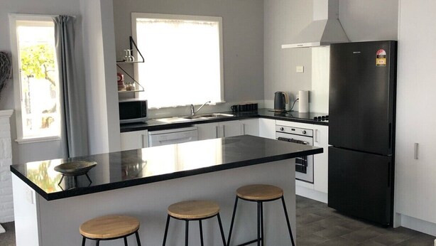 Une cuisine moderne dotée d’un îlot central, d’appareils électroménagers noirs et d’une fenêtre avec des rideaux.