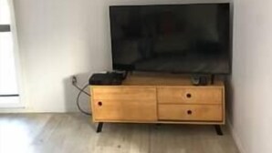 Een kamer met een houten tv-meubel, een flatscreen-televisie en een witte airconditioning die aan de muur is bevestigd.