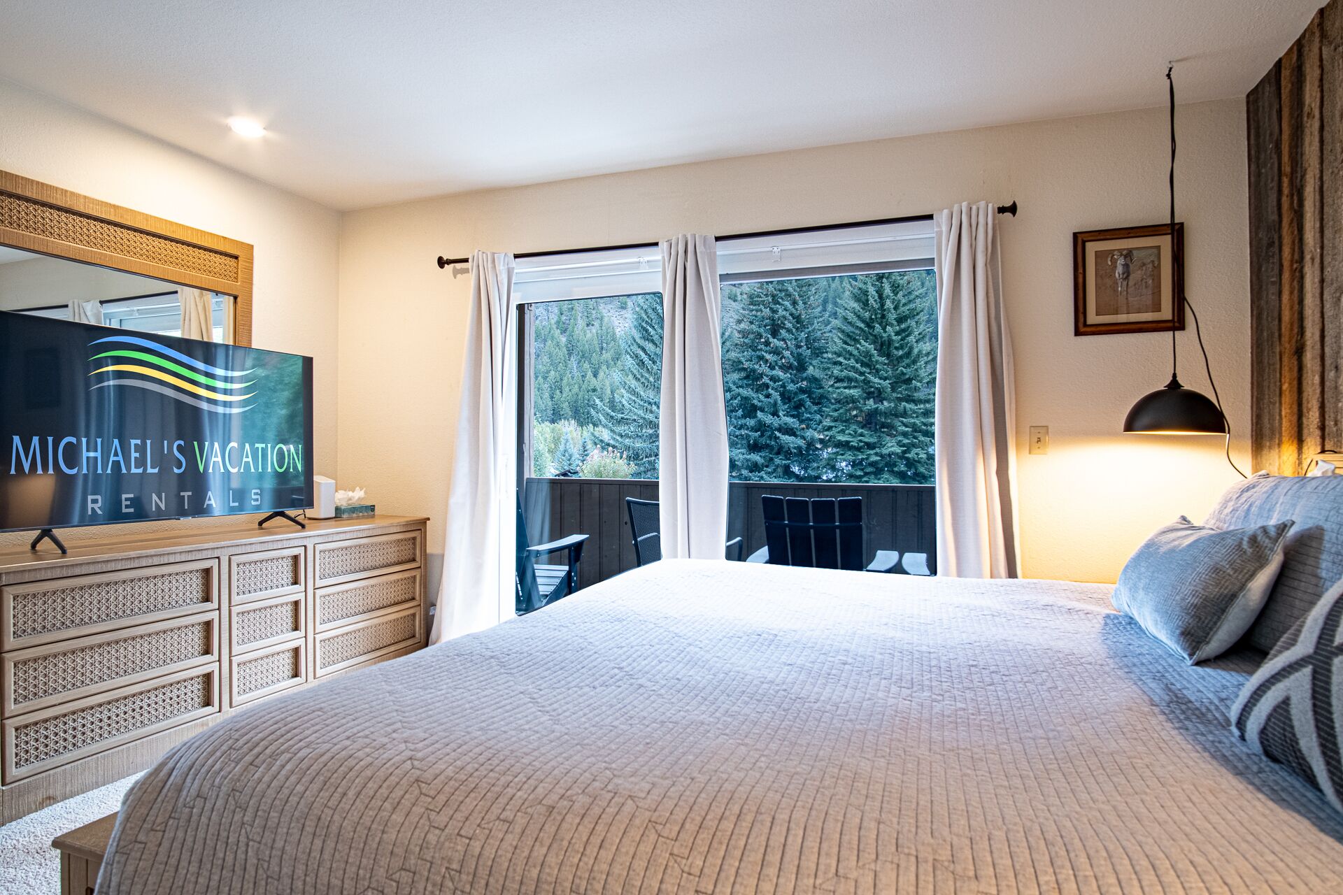 A bedroom with a large bed, a dresser, a TV, and a balcony with curtains.