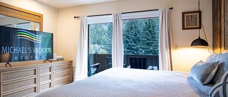 A bedroom with a large bed, a dresser, a TV, and a balcony with curtains.