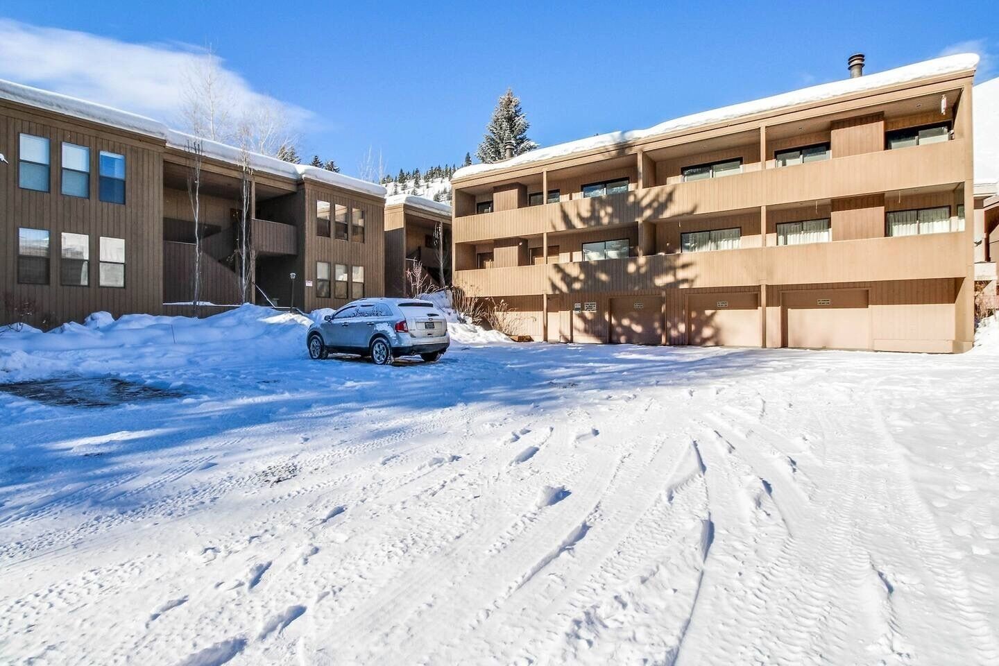 A building with a parking area covered in snow, a car parked in front, and a clear sky.