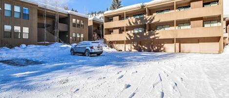 A building with a parking area covered in snow, a car parked in front, and a clear sky.