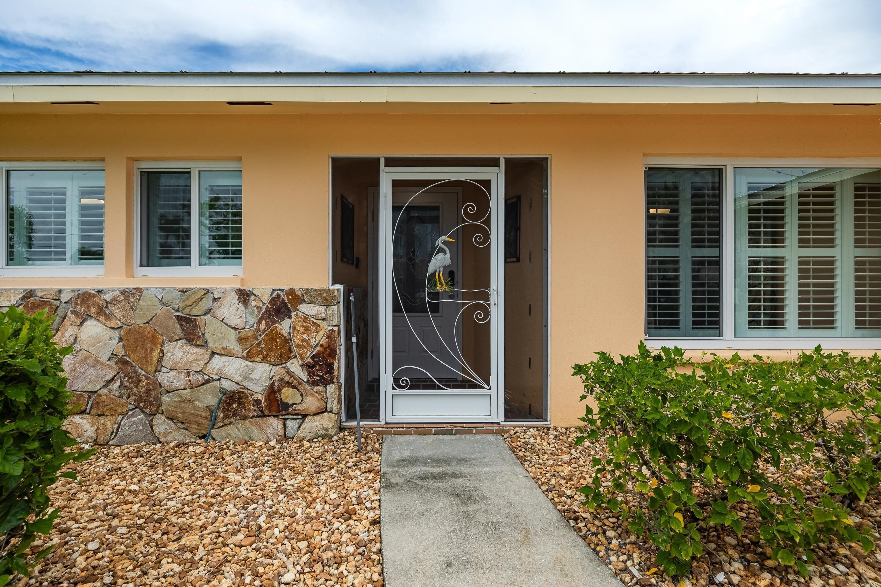 A modern house with a stone wall, a concrete pathway, and a door with a decorative metal design.