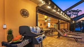 An outdoor patio with a grill, lounge chairs, and a dining area. - Yacht Club - Walk to Beach, Restaurant/Bar! Heated Saltwater Pool  - Villa Beachside Bliss - Roelens (Cape Coral)