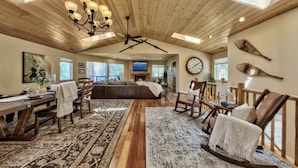 A spacious living area with a high ceiling, wooden beams, a large TV, and a dining area with a wooden table and chairs. - Lake Views and Mountain Luxury Lx66 (Zephyr Cove)