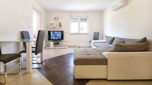 A modern living room with a glass dining table, two black chairs, a beige sofa, and a television. - Holiday apartment with WiFi and balcony (Medulin)