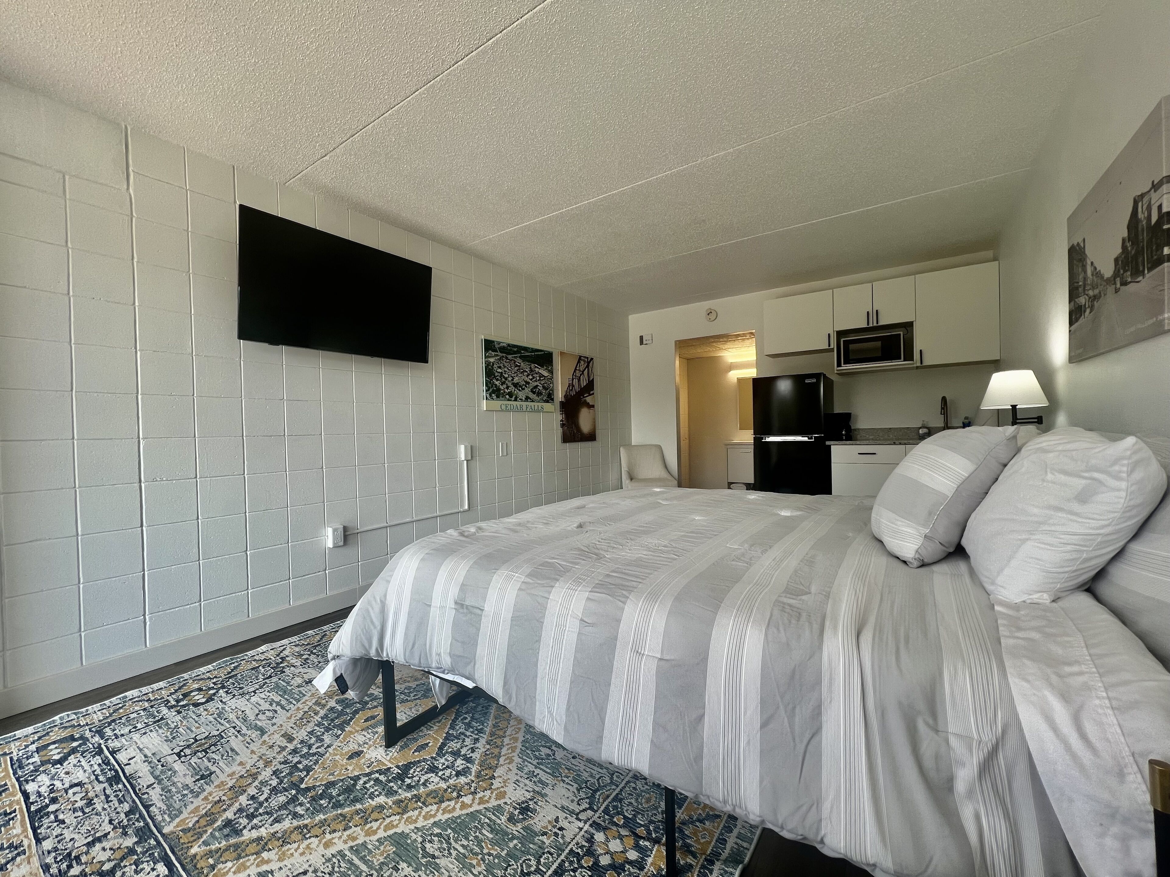 Ein Hotelzimmer mit Bett, einer kleinen Küchenzeile, einem Flachbildfernseher und einem gemusterten Teppich.