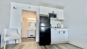 Una cucina compatta con mobili bianchi, un frigorifero nero, un forno a microonde e un lavello.