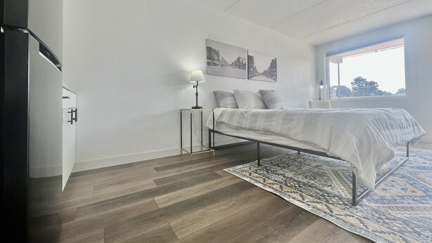 Una camera da letto con un letto, un comodino, una lampada, un tappeto e una finestra.