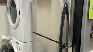 A compact kitchen with a stainless steel refrigerator and a front-loading washing machine. - Seaview Hideaway 2BR Near Alki Beach & Stadiums (Seattle)