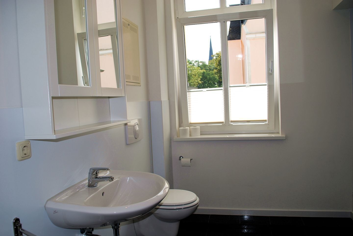 A bathroom with a white sink, toilet, and a window with blinds.