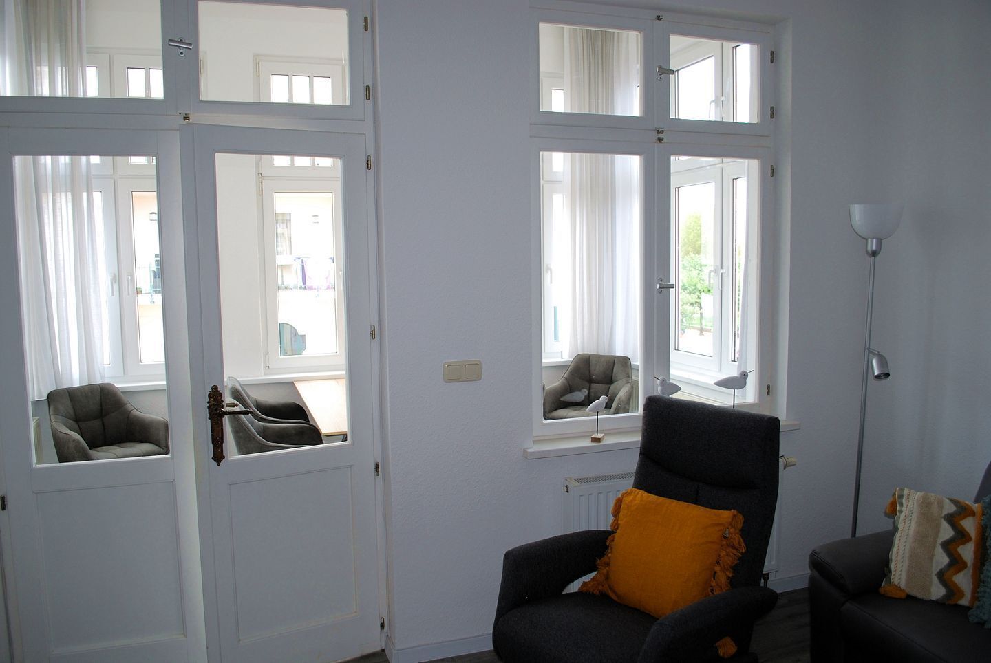 Een kamer met een groot raam, een stoel met een geel kussen en een vloerlamp.