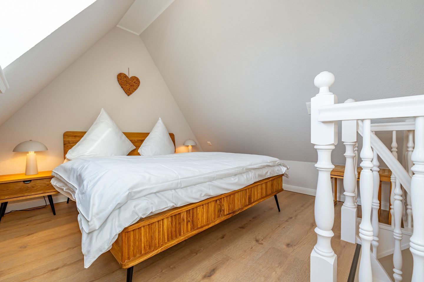 Ein Schlafzimmer mit einem hölzernen Bett, weißer Bettwäsche, einer herzförmigen Dekoration an der Wand und einer weißen Treppe.
