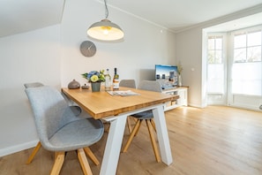 Un coin repas avec une table en bois, des chaises grises, une horloge et un téléviseur posé sur un meuble.