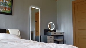 A bedroom with a bed, a dresser with drawers, a mirror with lights, and a door. - Beautiful Victorian home, Great view with balcony. Free parking. (Boston)