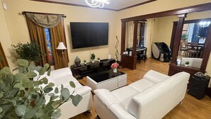 A living room with a white sofa, a flat-screen TV, a piano, and a massage chair. - Beautiful Victorian home, Great view with balcony. Free parking. (Boston)