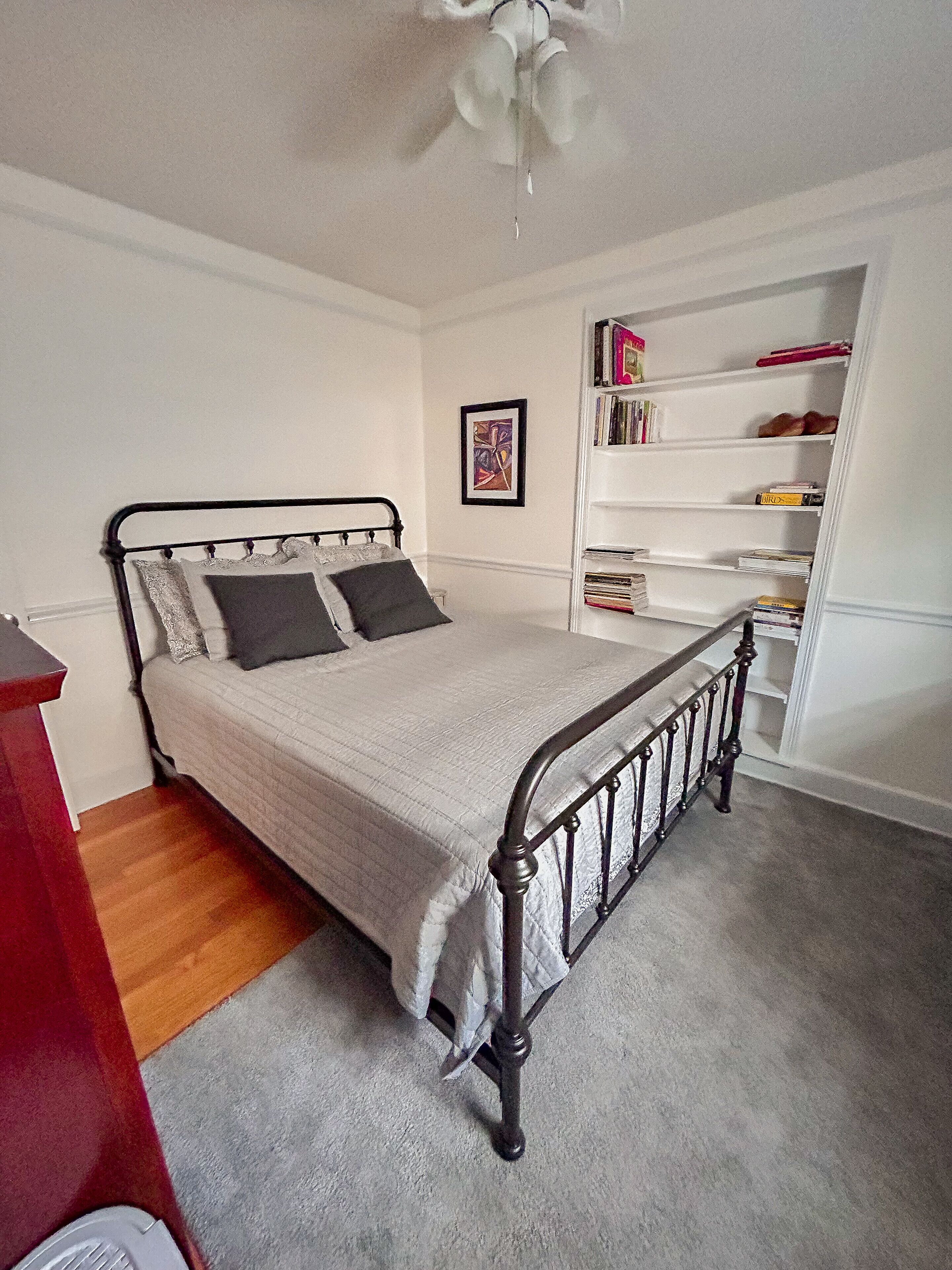 A neatly arranged bedroom with a bed, a bookshelf, and a ceiling fan.