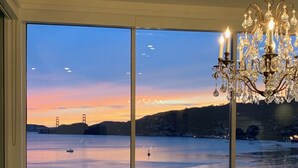 A dining area with a view of a large body of water, a chandelier, and wicker furniture. - Stunning Panoramic views of SF, Bay/GG Bridge, Sausalito, Mt. Tam in  Belvedere (Belvedere)
