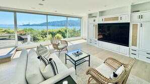 A modern living room with a large TV, white cabinetry, and a view of a body of water. - Stunning Panoramic views of SF, Bay/GG Bridge, Sausalito, Mt. Tam in  Belvedere (Belvedere)