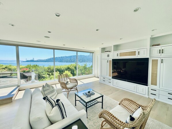 A modern living room with a large TV, white cabinetry, and a view of a body of water.