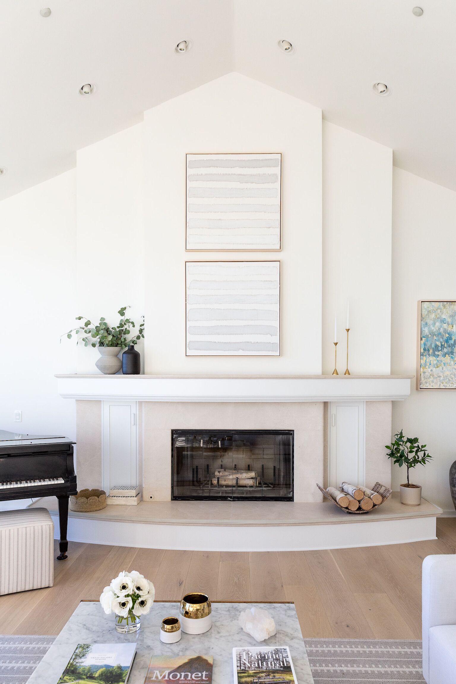 A living room with a fireplace, a piano, and a coffee table with books and flowers.