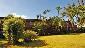 A hotel with a red exterior, a grassy lawn, and several palm trees. - Wonderful Honokowai Beach Condos (Lahaina)