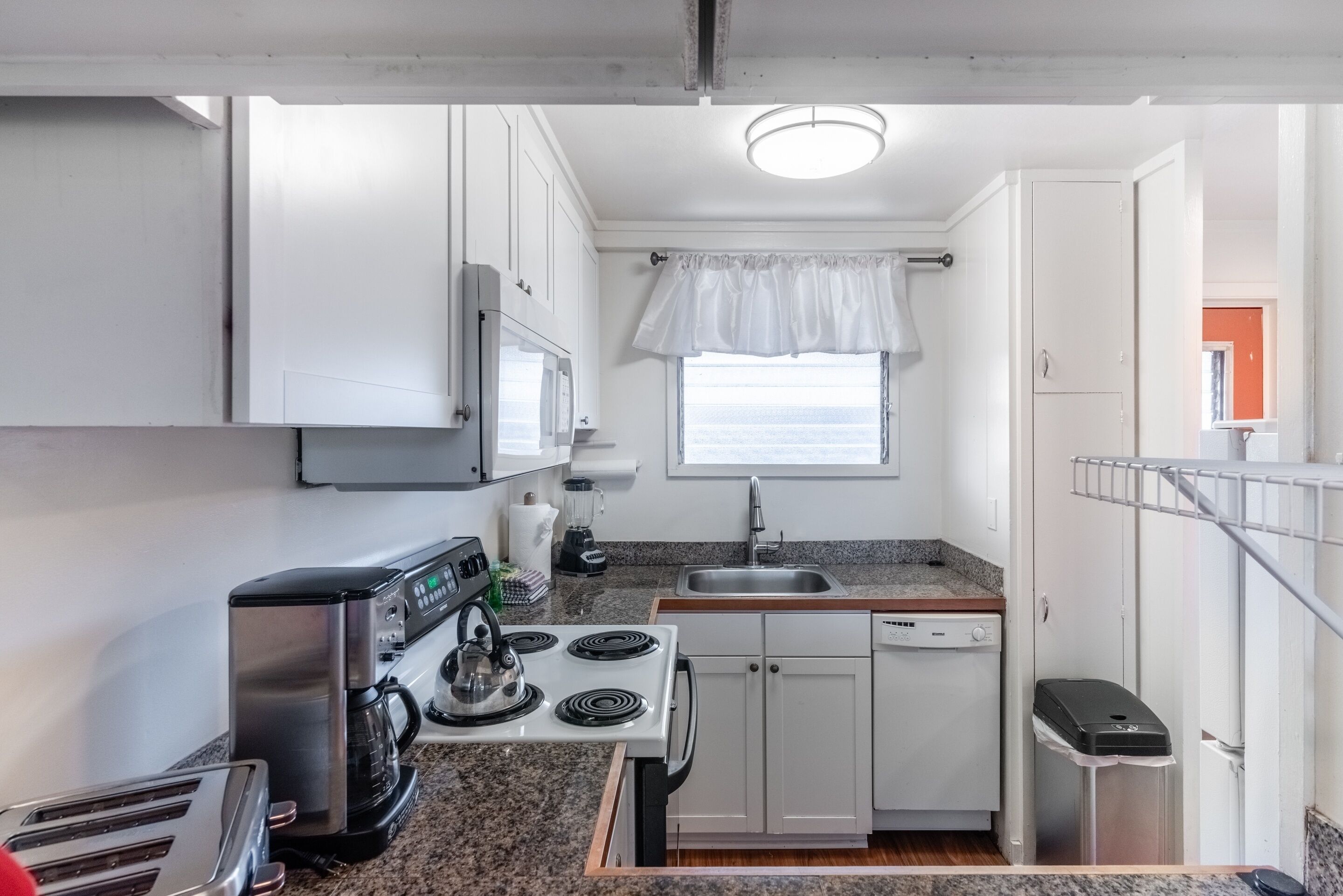 A compact kitchen with white cabinets, a stove, a sink, and a window with a view.