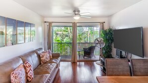 A spacious living area with a sofa, chairs, a flat-screen TV, and a balcony with a view of greenery. - Wonderful Honokowai Beach Condos (Lahaina)