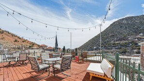 A wooden deck with outdoor seating, string lights, and a view of a hill and buildings.