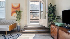 Ein modernes Wohnzimmer mit einer Couch, einem Topf mit Pflanze, einer Treppe, die zu einem Balkon führt, und einem Fernseher auf einer Holzkommode.
