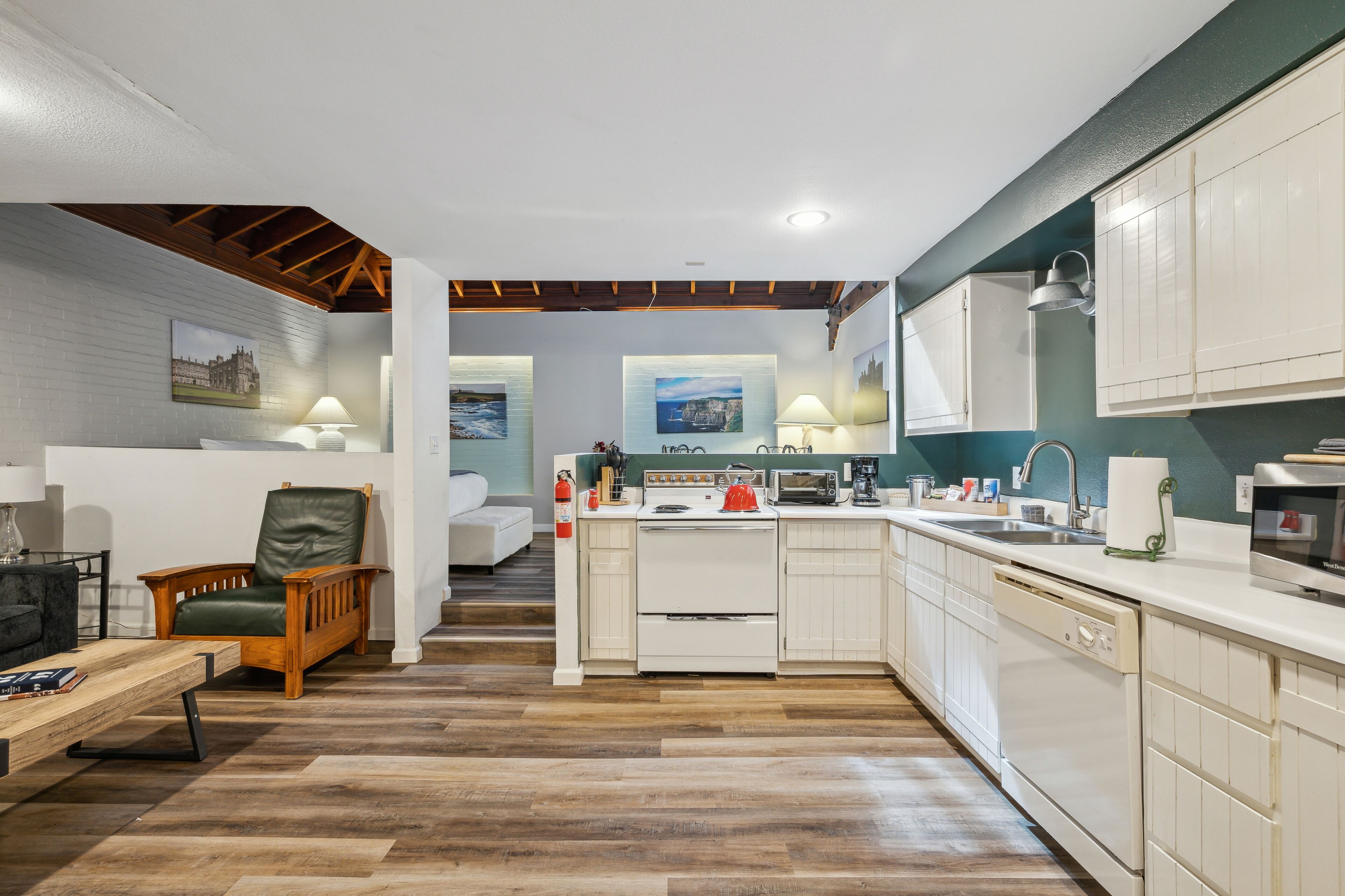 A compact kitchen with white cabinets, a wooden chair, a dining table, and a view of the living room.