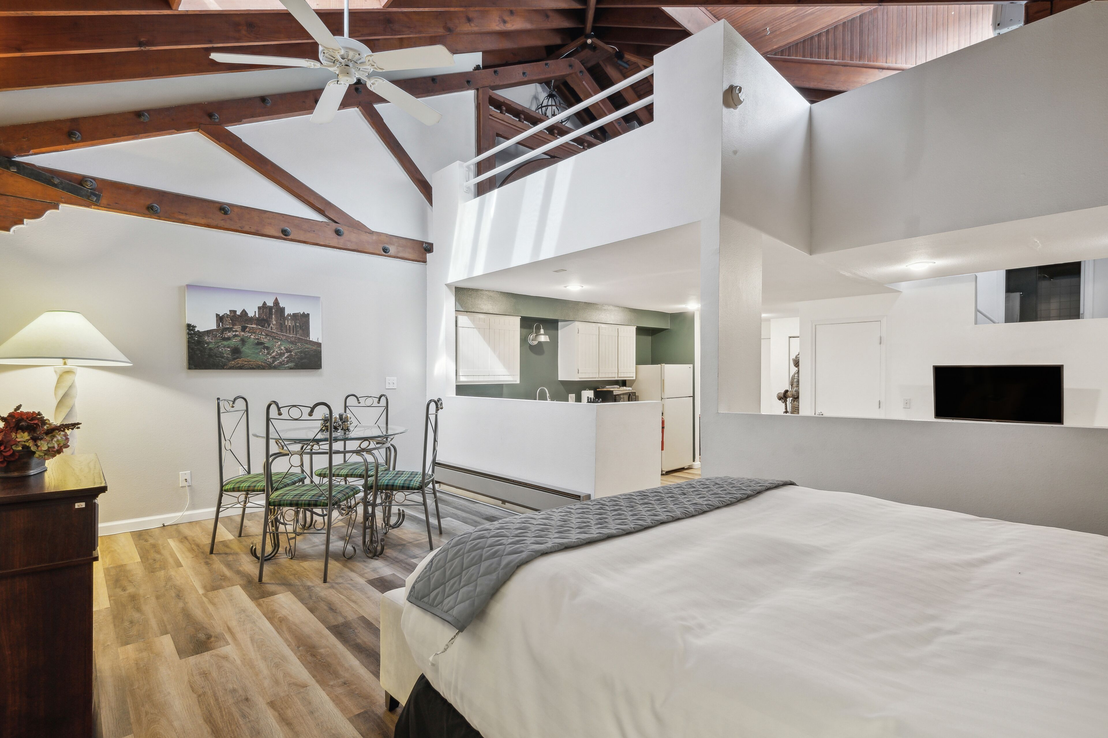 Ein Schlafzimmer mit einem Bett, einem Schreibtisch, einem Stuhl und einem Esstisch. Im Hintergrund befindet sich eine Küchenzeile.