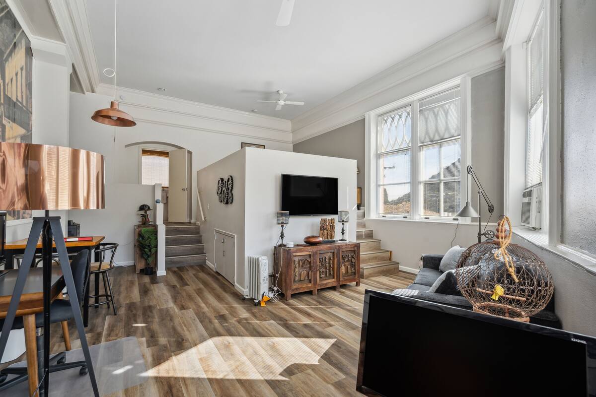 A spacious living room with a large flat-screen TV, wooden flooring, and a cozy seating area with a sofa and a decorative birdcage.