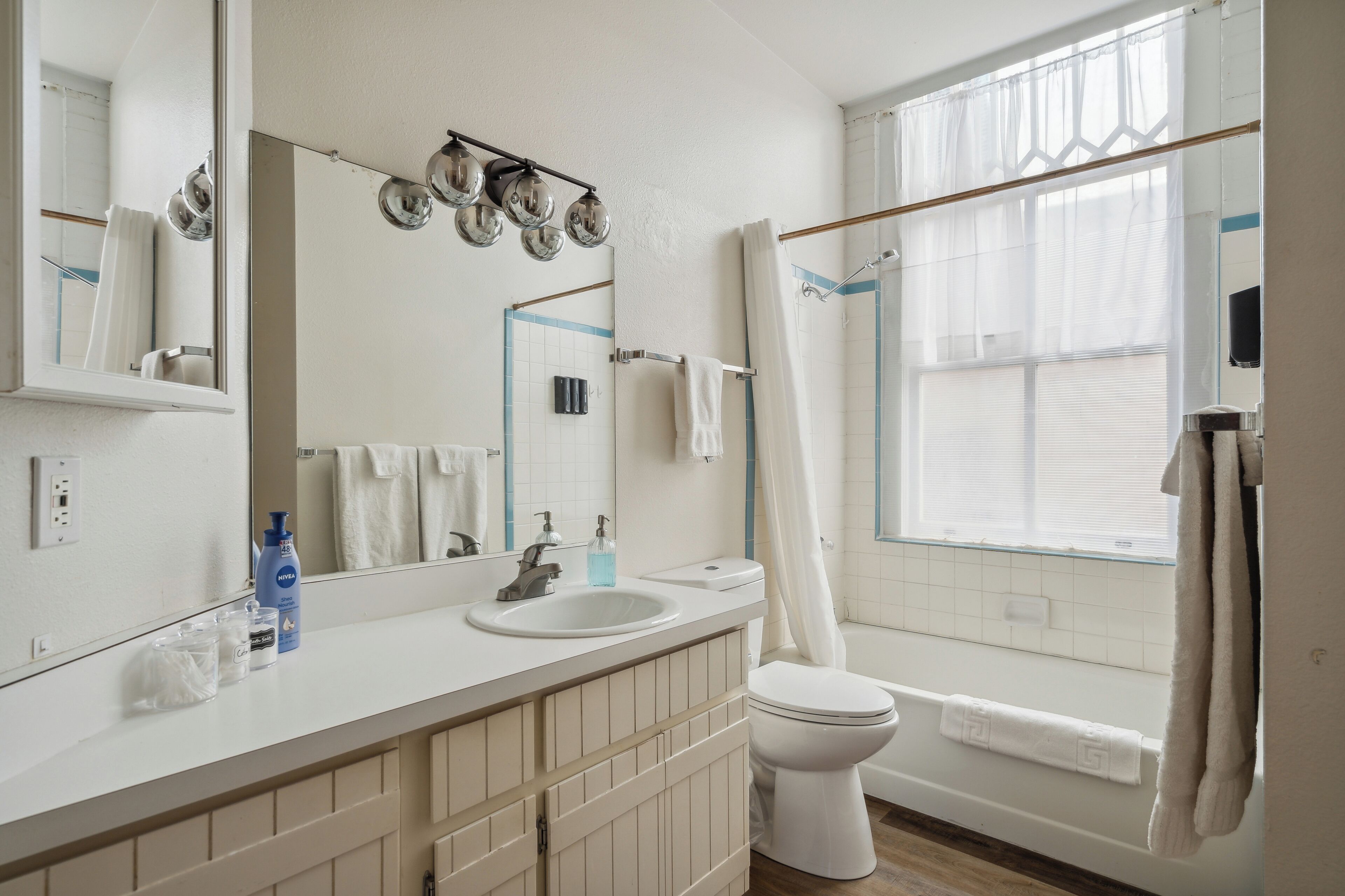 A bathroom with a white sink, mirror, and toilet. There are two bottles on the sink counter, a towel rack, and a shower curtain.