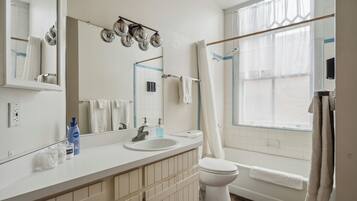 A bathroom with a white sink, mirror, and toilet. There are two bottles on the sink counter, a towel rack, and a shower curtain.