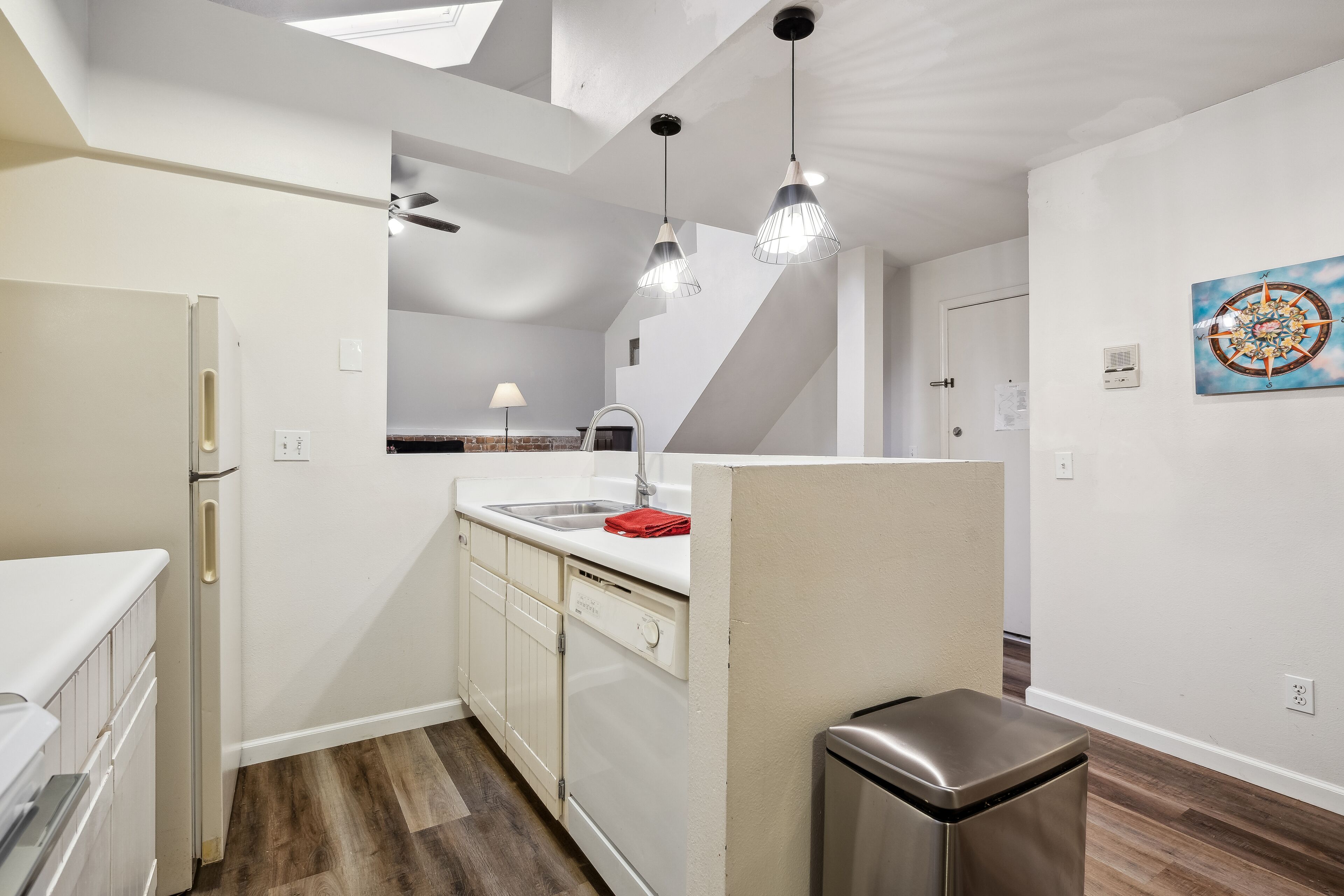 A modern kitchen with white cabinetry, a stainless steel refrigerator, and pendant lighting.