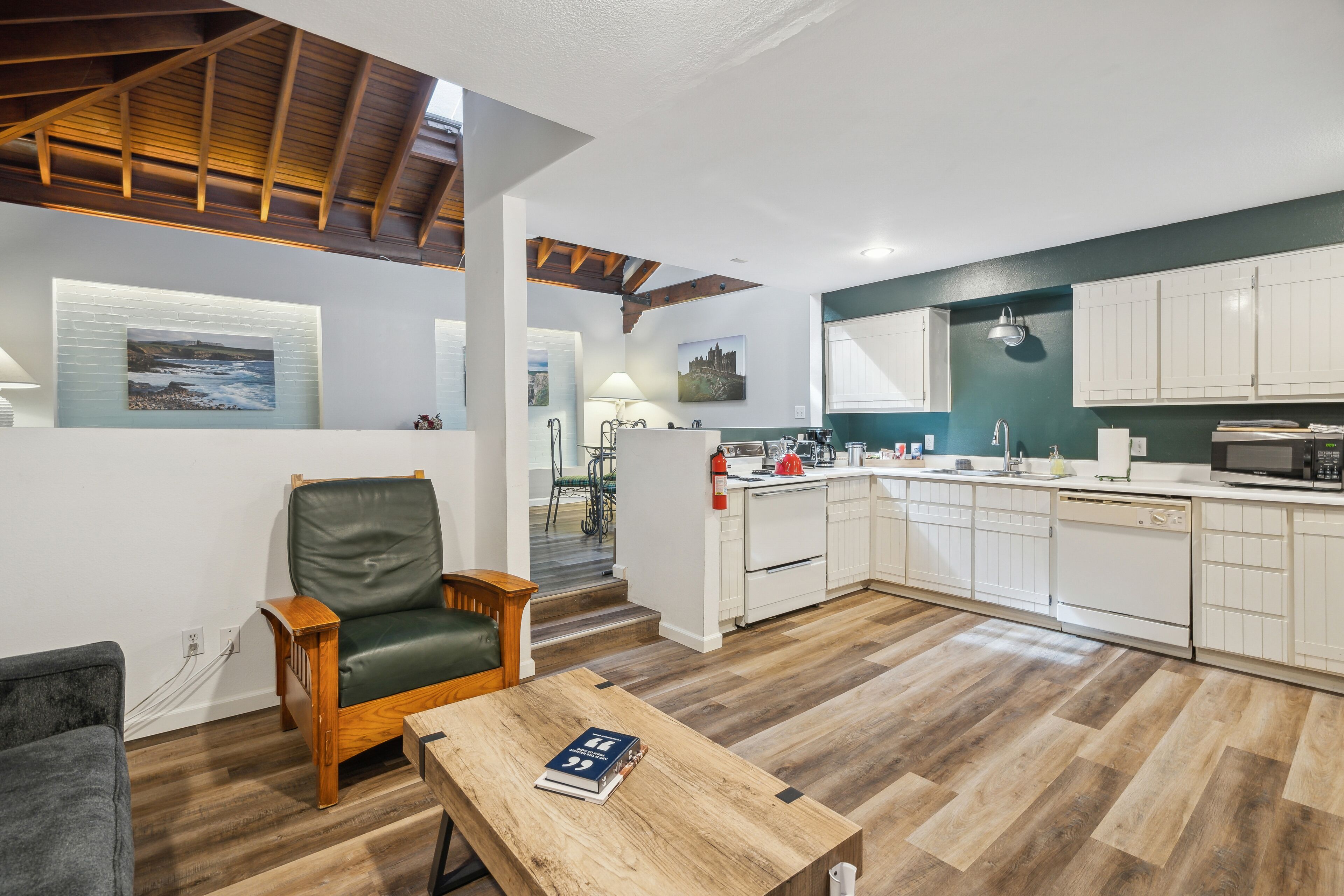 A modern kitchen with white cabinets, a wooden dining table, and a green accent wall.