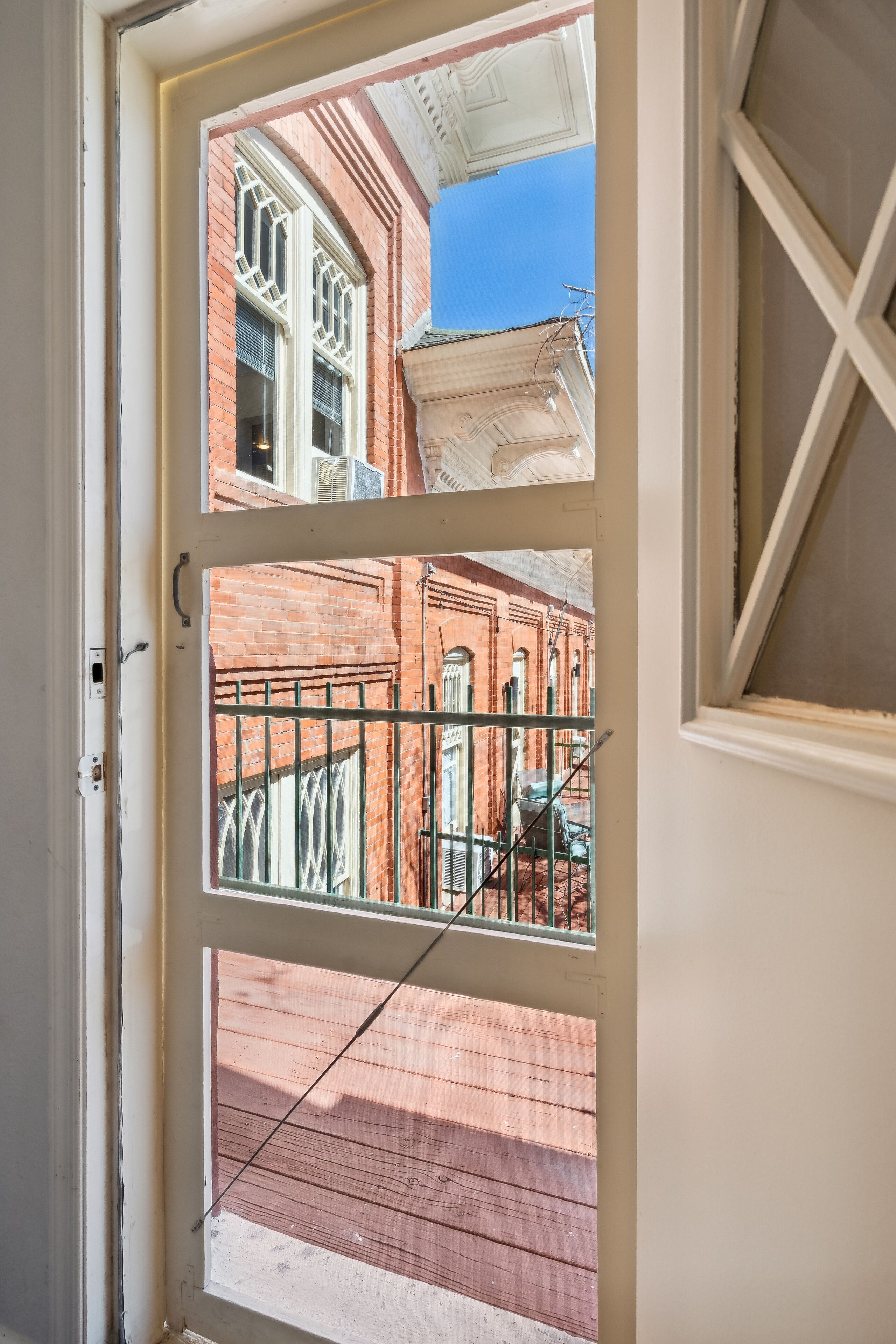 A view through a door with a metal gate and a brick building in the background.