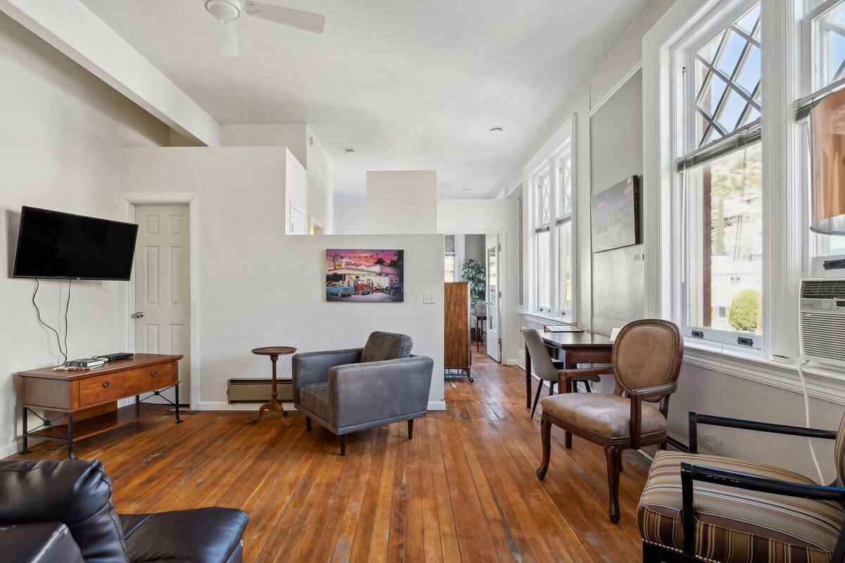 A spacious living room with hardwood flooring, a flat-screen TV mounted on the wall, and a dining area with wooden furniture.