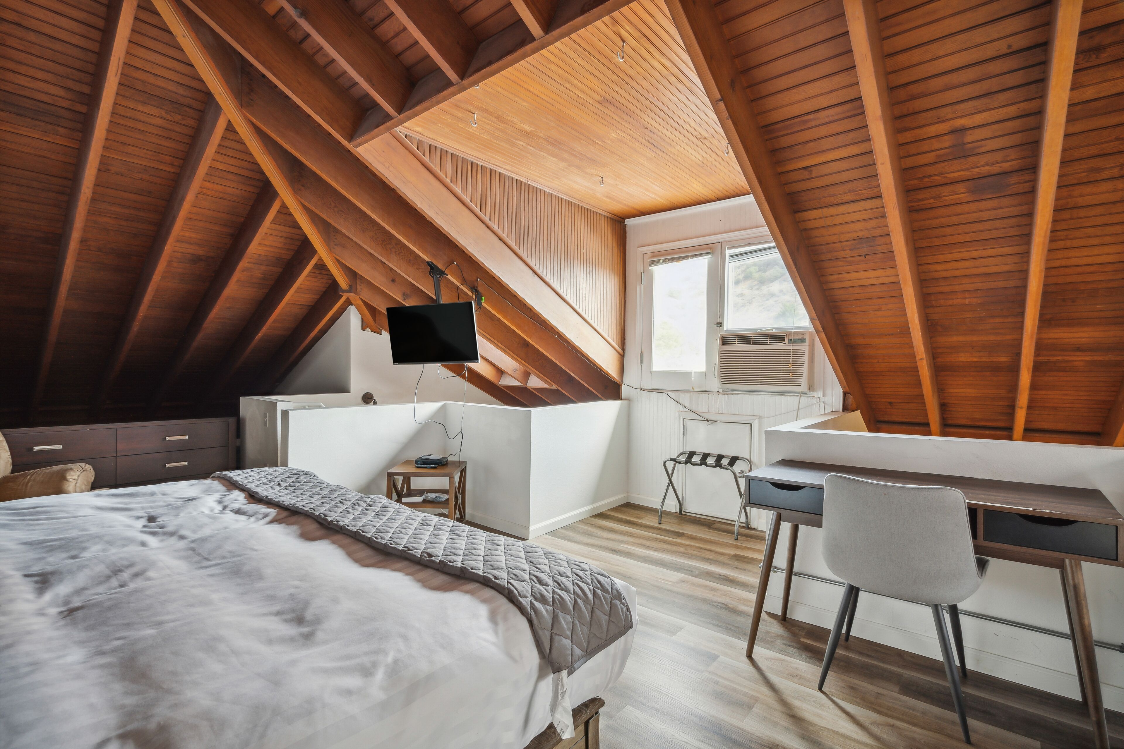 Un dormitorio con techo estilo loft, una cama, un escritorio y una silla.